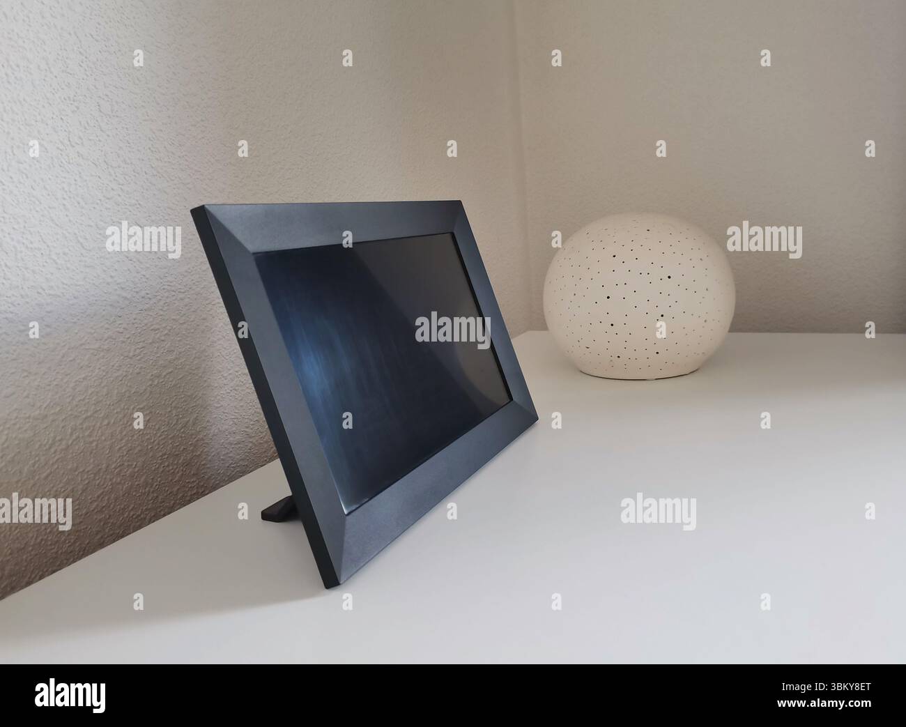 Mockup con cornice fotografica digitale nera con spazio di copia su un piano di lavoro bianco con lampada sferica decorativa Foto Stock