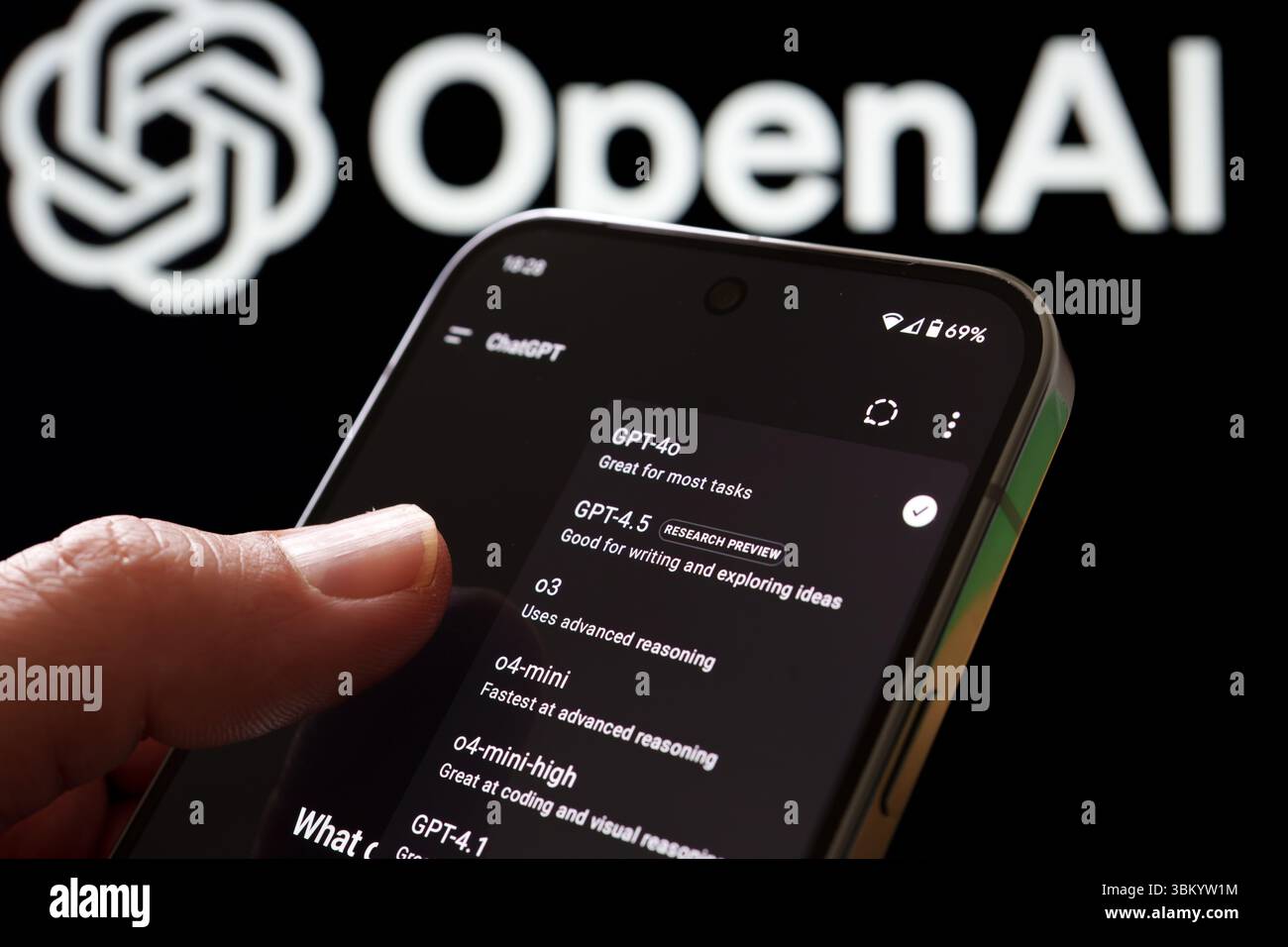 Utente che interagisce con il selettore del modello ChatGPT sul telefono con il logo OpenAI dietro. Stafford, Regno Unito, 23 giugno 2025 Foto Stock