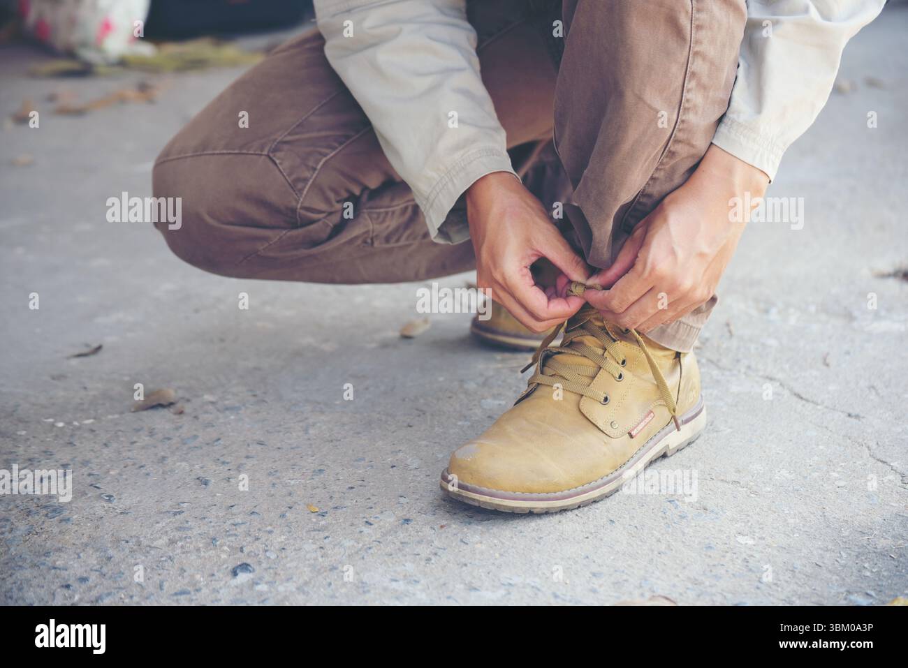 Stivali industriali uomo inginocchiati e cravatta per lavoratori. Primo piano di un uomo con le mani legate per i suoi stivali marroni da costruzione. Primo piano, han Foto Stock