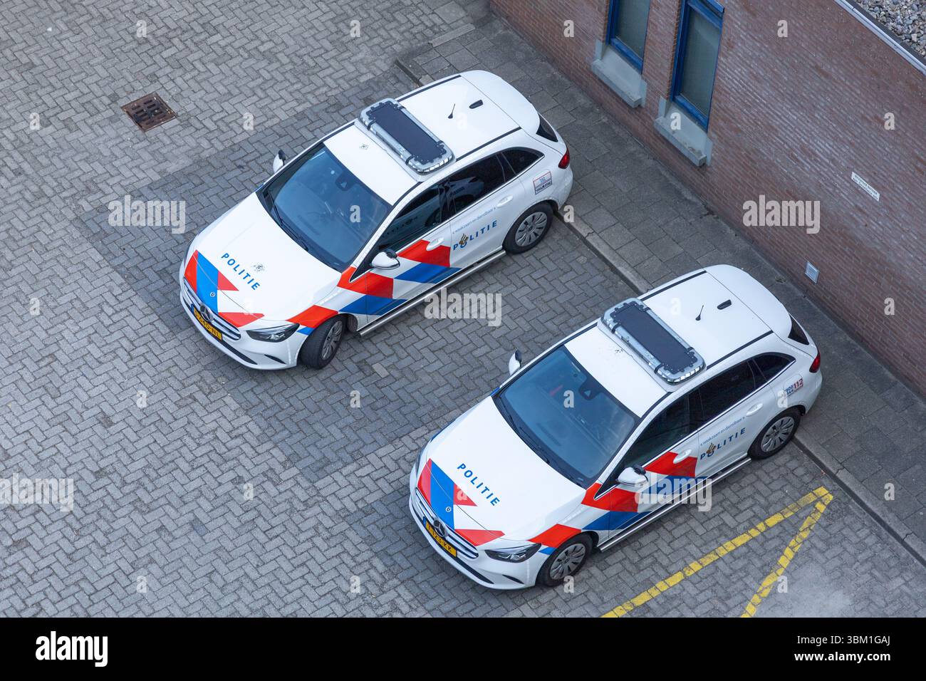 Vista aerea di due auto della polizia olandese ("Politie") parcheggiate su una superficie di mattoni. Utrecht, Paesi Bassi. 15 aprile 2025. Foto Stock