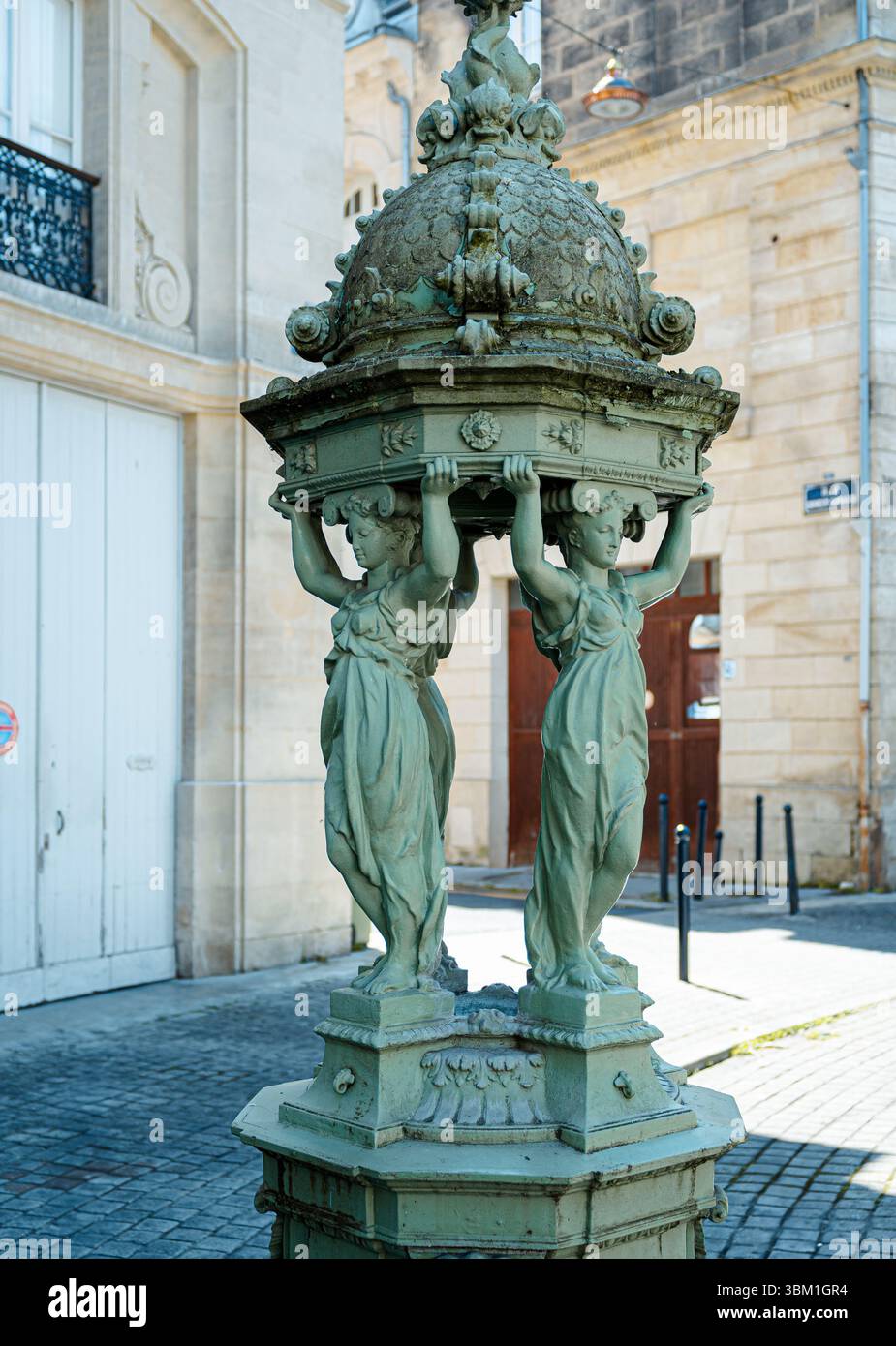 Una fontana Wallace in ghisa verde vintage, con cariatidi che sostengono una cupola, si erge su una strada europea acciottolata Foto Stock