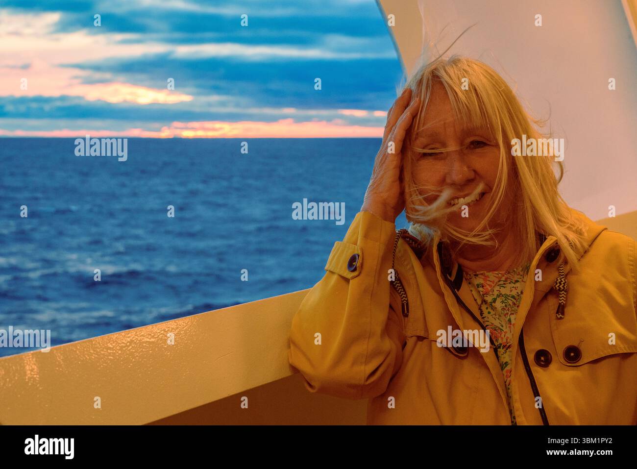 Donna sulla nave da crociera nel Circolo Polare Artico con sole di mezzanotte alle spalle, vento che soffia capelli sul viso. Foto Stock