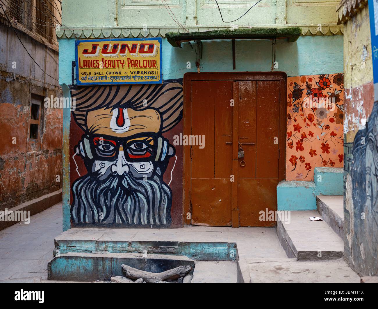 India, Varanasi, 16 marzo 2025. Il colorato murale di un saggio barbuto adorna la facciata del "Juno Ladies Beauty Parlour" in una tranquilla strada secondaria di Varanasi Foto Stock