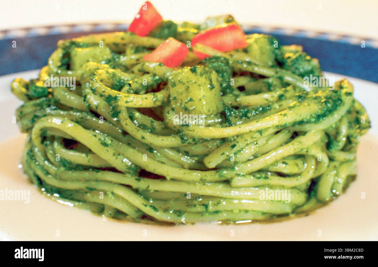 Tradizionale trenette italiana condita con pesto e guarnita con pomodori a dadini e patate, servita su un piatto bianco e blu Foto Stock