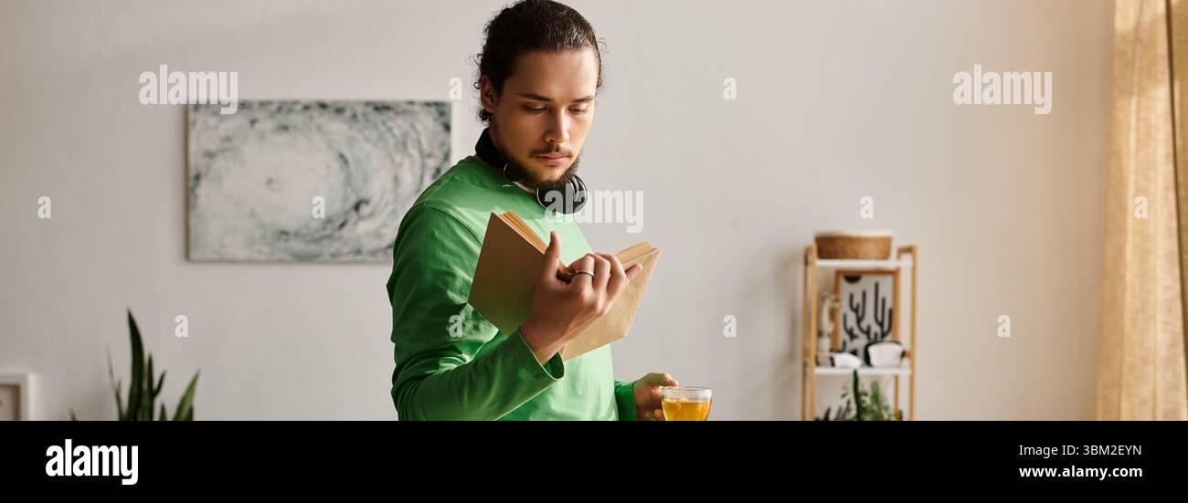 Un giovane si trova nel suo accogliente spazio abitativo, impegnato a leggere un libro con un drink in mano. Foto Stock