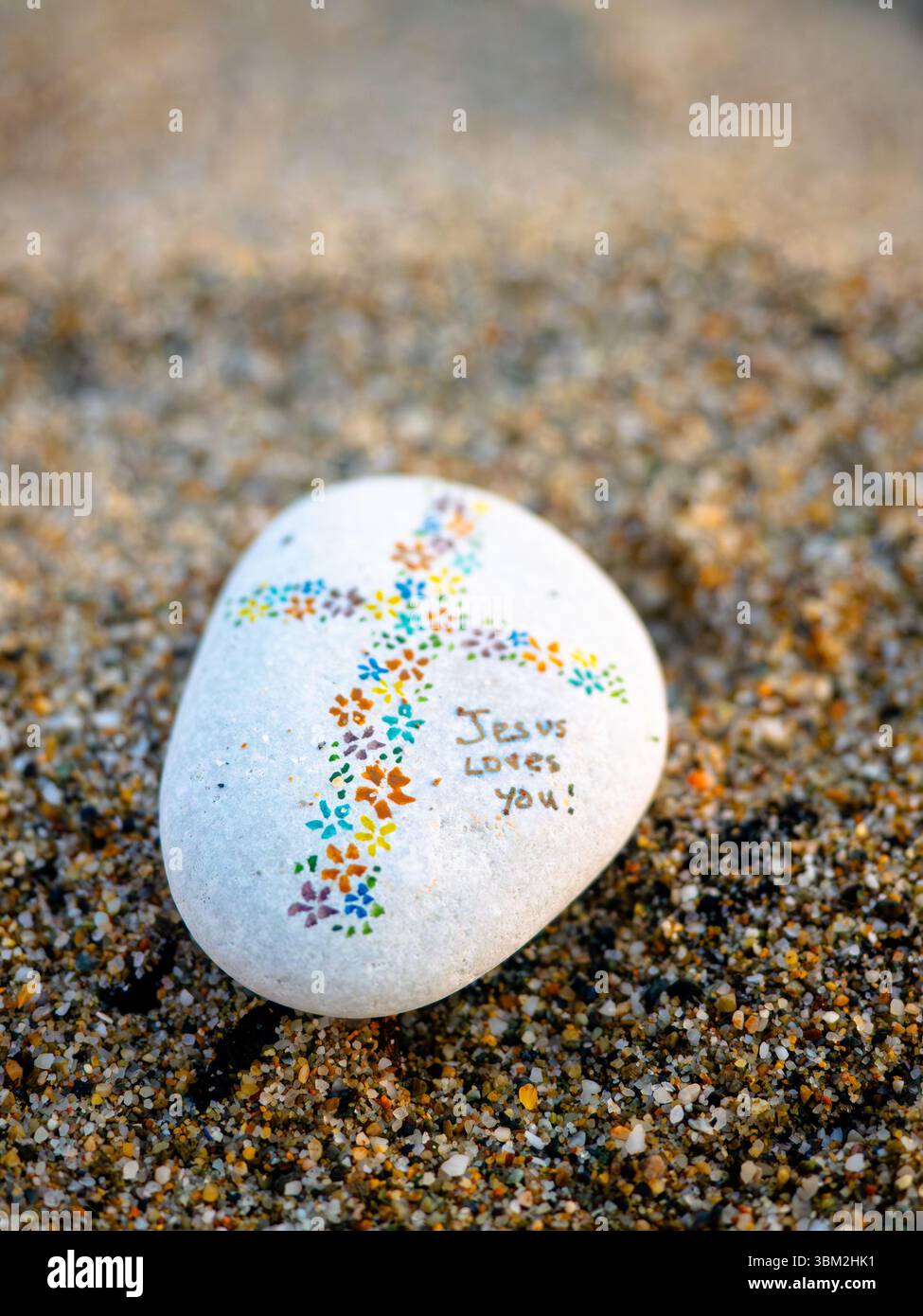 Ispiratrice pietra dipinta con colorato disegno a croce sulla sabbia della spiaggia che crea speranza e messaggio di fede Foto Stock
