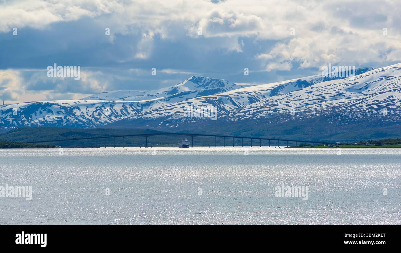 Costa norvegese con nave che passa sotto un ponte, vicino a Tromso, Norvegia, a giugno Foto Stock