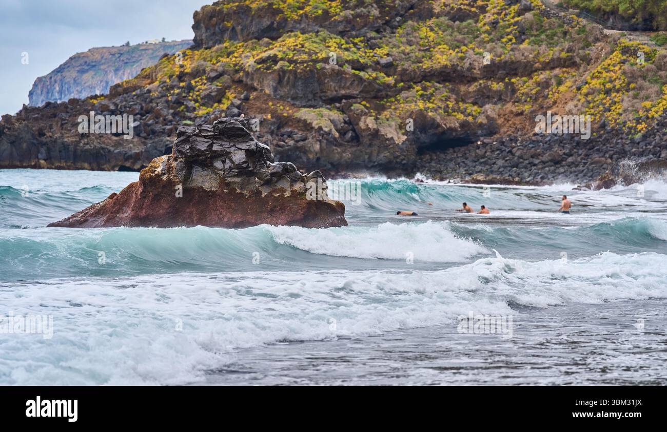 Formazione di rocce vulcaniche nella zona del surf con nuotatori che si godono le onde della spiaggia di El Bollullo a Tenerife Foto Stock