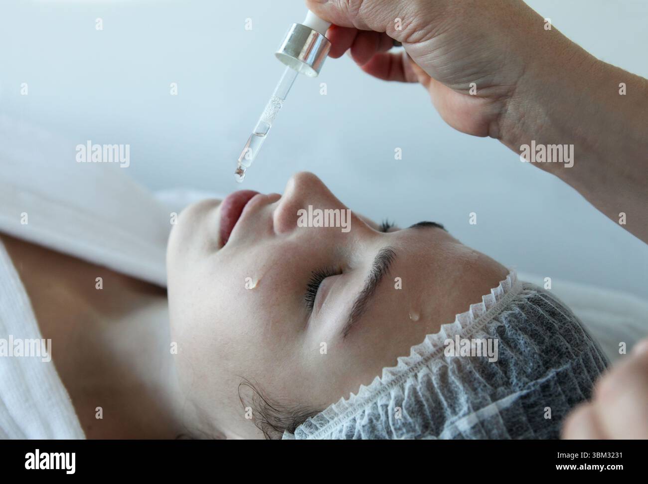 donna che riceve un trattamento per la cura della pelle in una spa di bellezza o in una clinica estetica, con un estetista che applica olio o siero per il viso Foto Stock