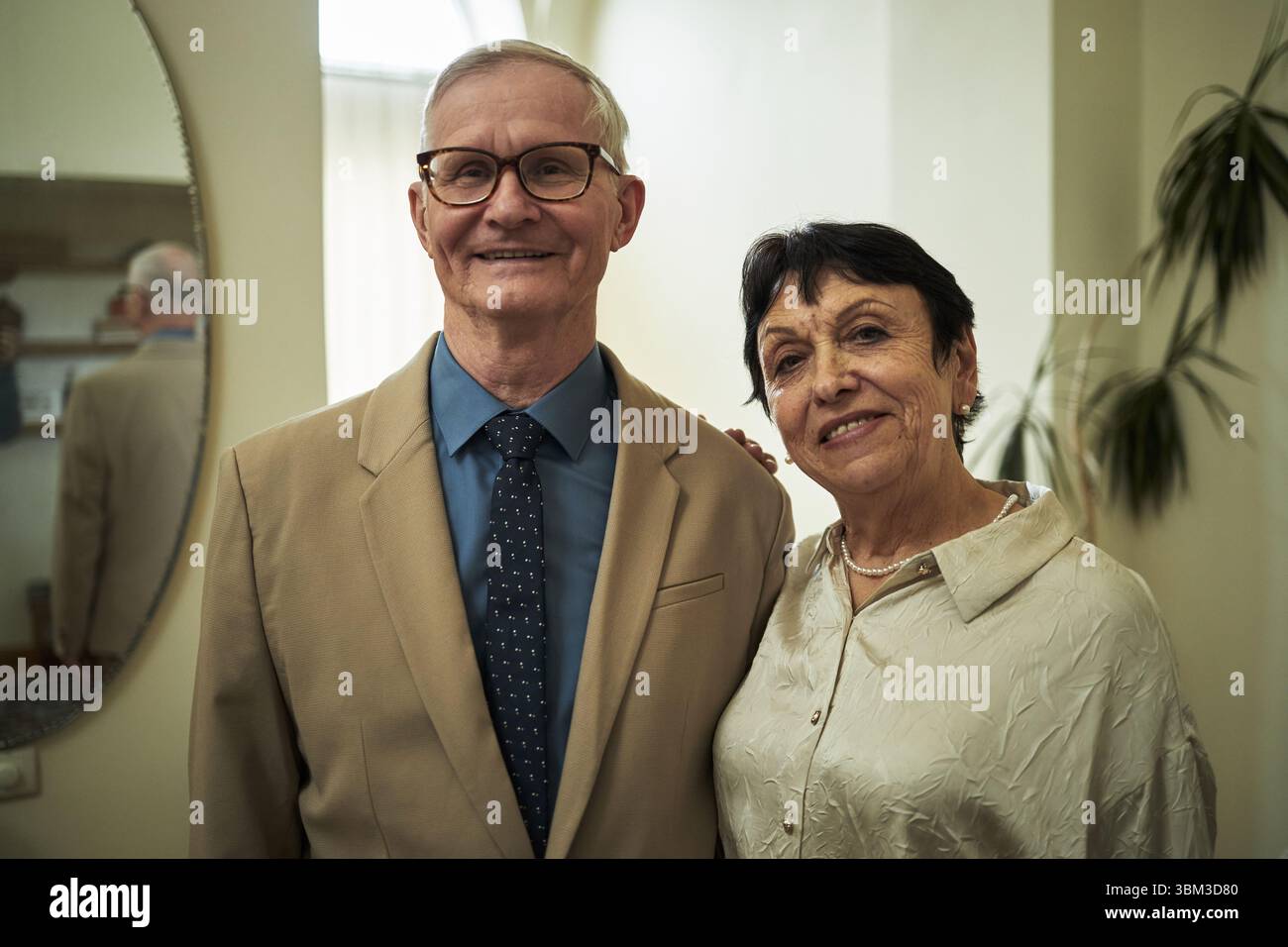 Ritratto di coppie anziane sorridenti e in piedi in casa con espressioni rilassate, elegantemente vestite per feste o concerti. Il gentiluomo indossa un abito mentre la signora indossa una camicetta Foto Stock