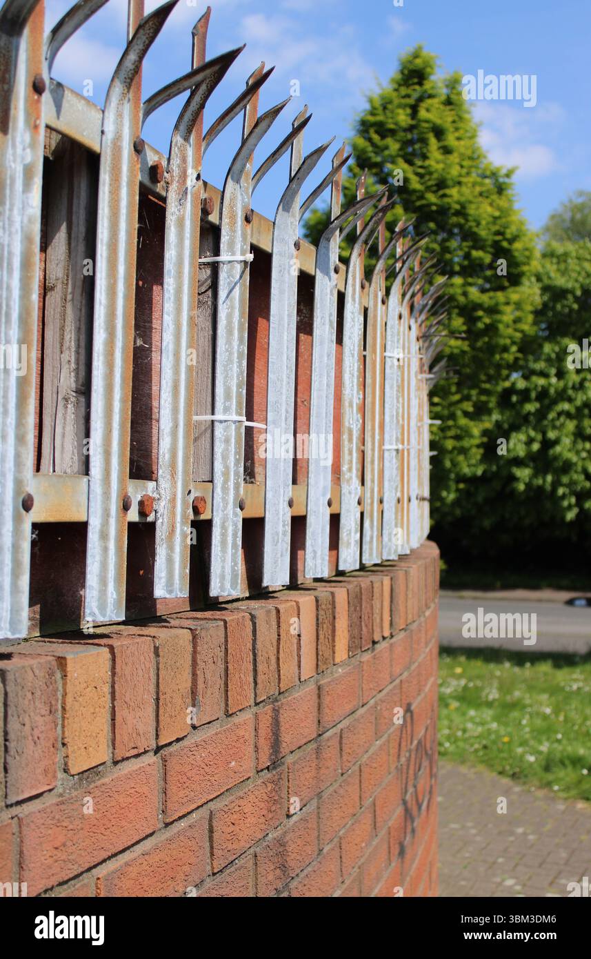 Muro di pace in mattoni dell'epoca dei problemi con punte metalliche appuntite e piegate in cima nel quartiere Shankill Road di Belfast, Irlanda del Nord Foto Stock