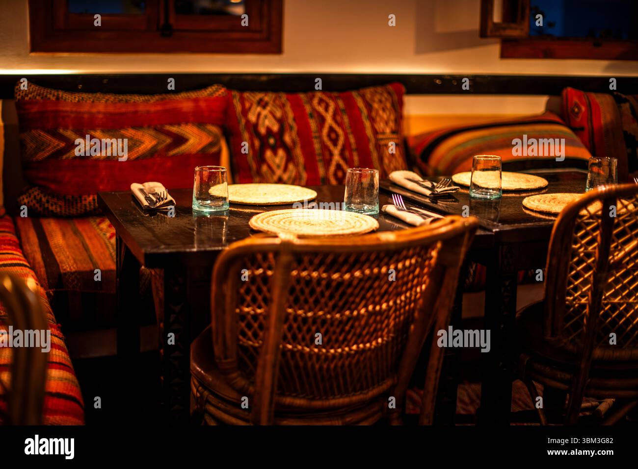 Tavolo per due con cuscini marocchini e sedie in vimini all'interno di un locale storico di Marrakech Foto Stock
