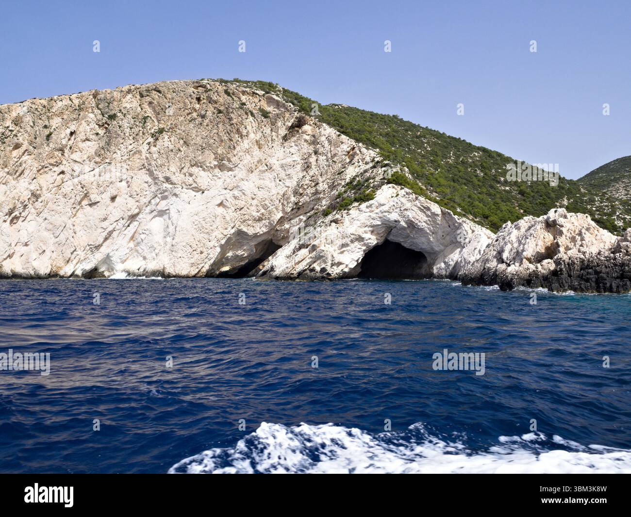 Iconiche scogliere calcaree dell'isola di Zante che si innalzano sopra il mare azzurro, con piccole grotte e flora mediterranea. Foto Stock