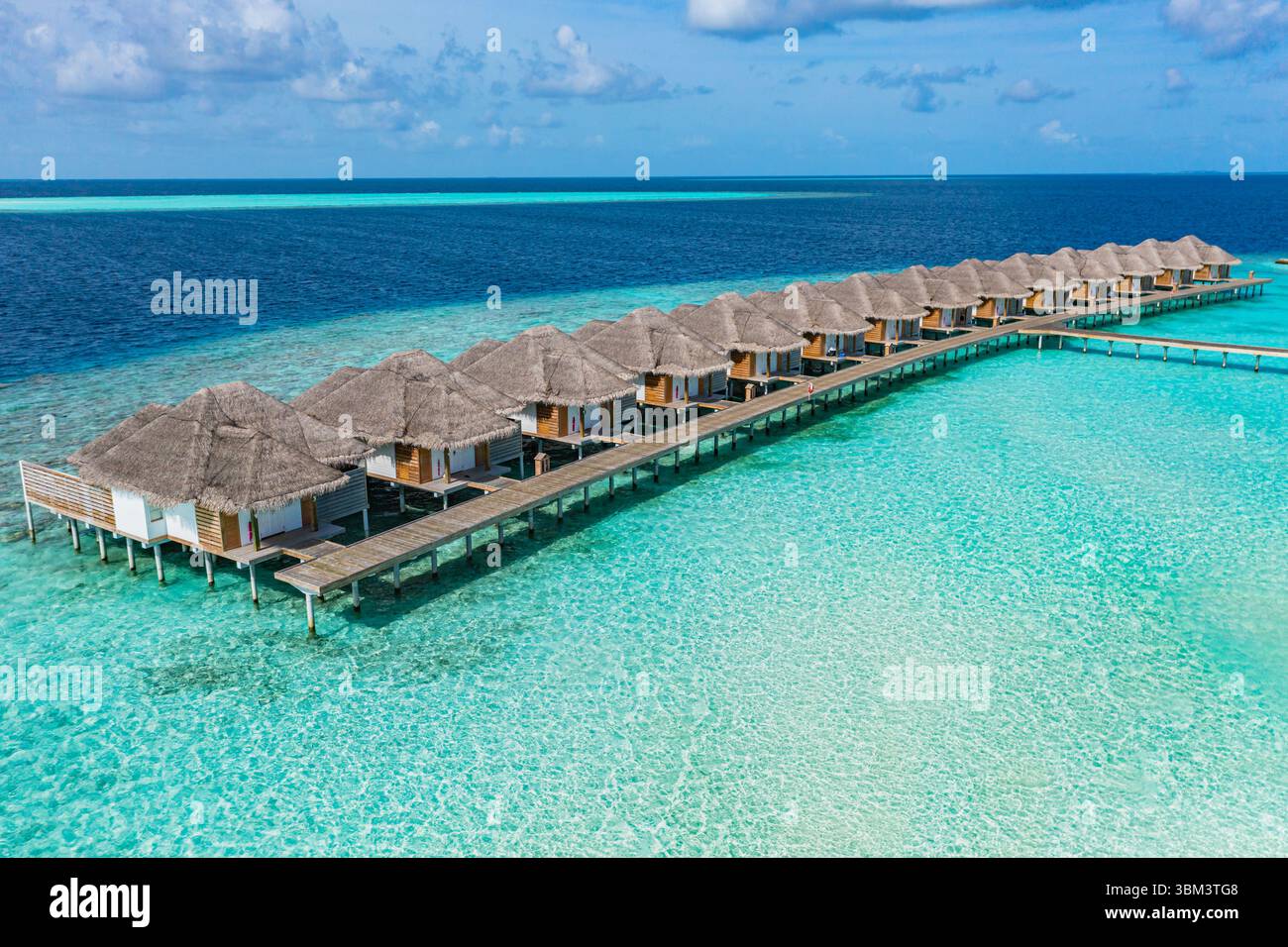 Incredibile vista aerea delle ville sull'acqua delle Maldive, che mostra il resort tropicale dell'isola, il mare turchese, la spiaggia sabbiosa e il cielo blu, una perfetta vacanza estiva Foto Stock