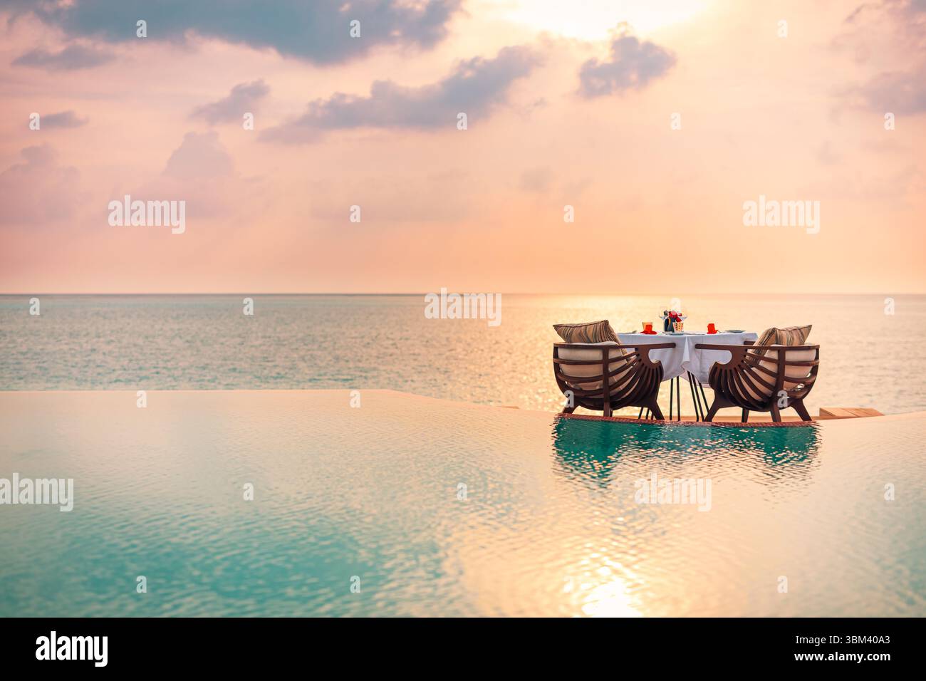 Romantica cena a bordo piscina al tramonto sul mare con tavolo sedie a lume di candela vista mare resort di lusso vacanze estive tropicali anniversario della luna di miele Foto Stock