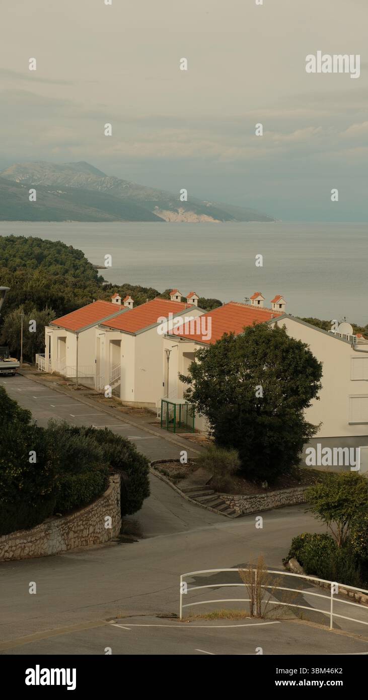 Una fila di case sul mare bianche perfettamente allineate con tetti di tegole arancioni si estende lungo una strada tranquilla sopra la costa adriatica. Foto Stock
