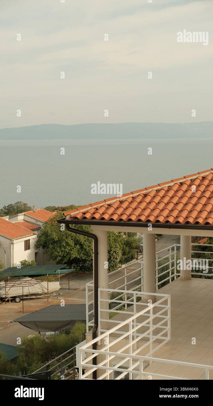 Una terrazza soleggiata si affaccia sul tranquillo Mare Adriatico, con ringhiere bianche che tracciano la geometria pulita del balcone. Foto Stock
