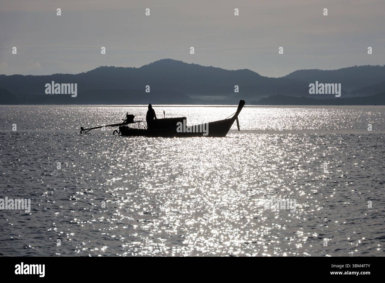 Silhouette di pescatore in barca da pesca con motore nel mare delle Andamane sullo sfondo della costa montana Foto Stock