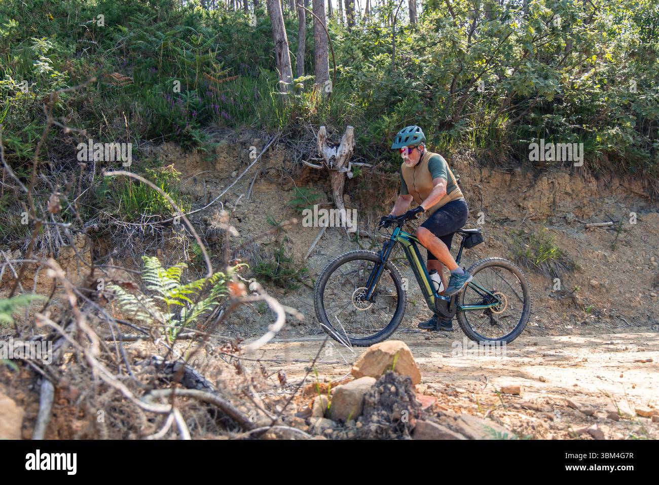 Uomo anziano attivo in sella a una mountain bike elettrica lungo un percorso nella foresta illuminato dal sole, abbracciando uno spirito avventuroso mentre si gode i benefici di una guarigione Foto Stock