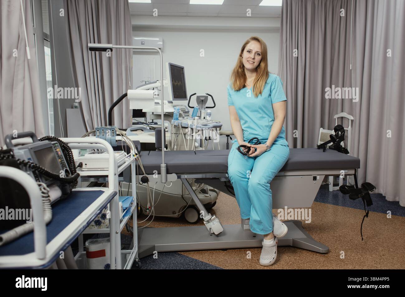 Ritratto di donna medico o ecografo in scrub in piedi nella moderna sala diagnostica a ultrasuoni con attrezzature mediche e stetoscopio. Foto Stock