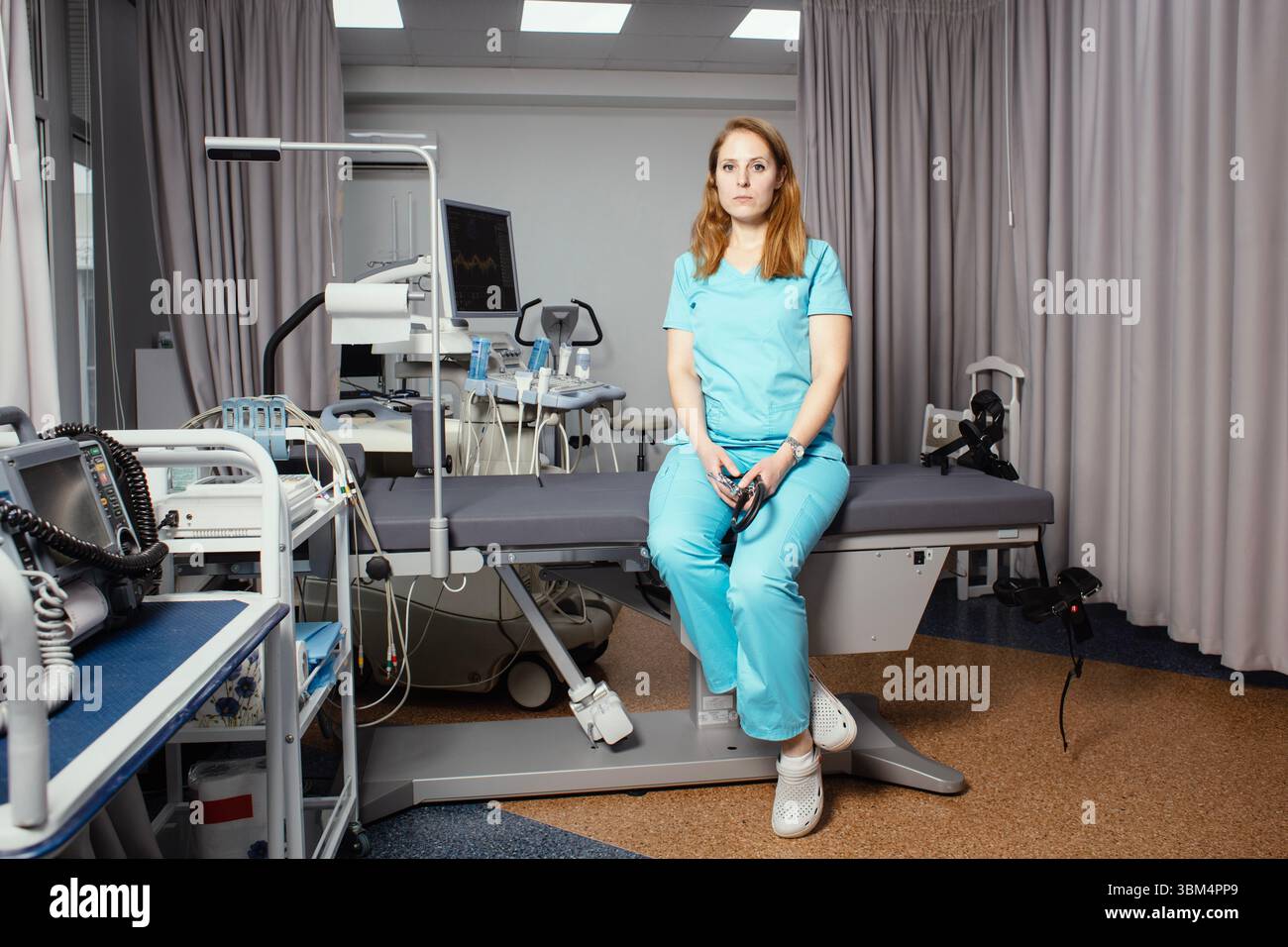 Ritratto di donna medico o ecografo in scrub in piedi nella moderna sala diagnostica a ultrasuoni con attrezzature mediche e stetoscopio. Foto Stock