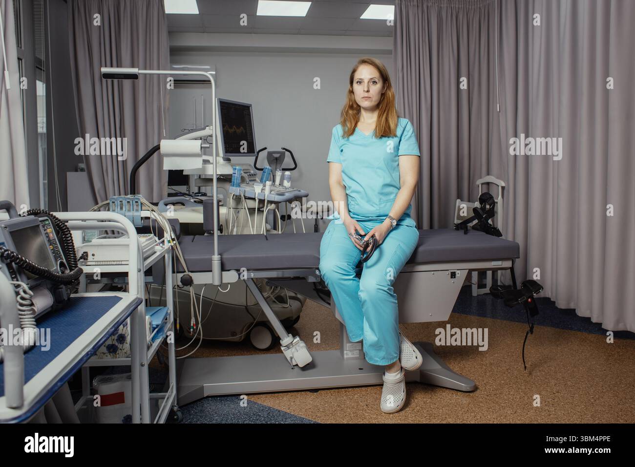 Ritratto di donna medico o ecografo in scrub in piedi nella moderna sala diagnostica a ultrasuoni con attrezzature mediche e stetoscopio. Foto Stock