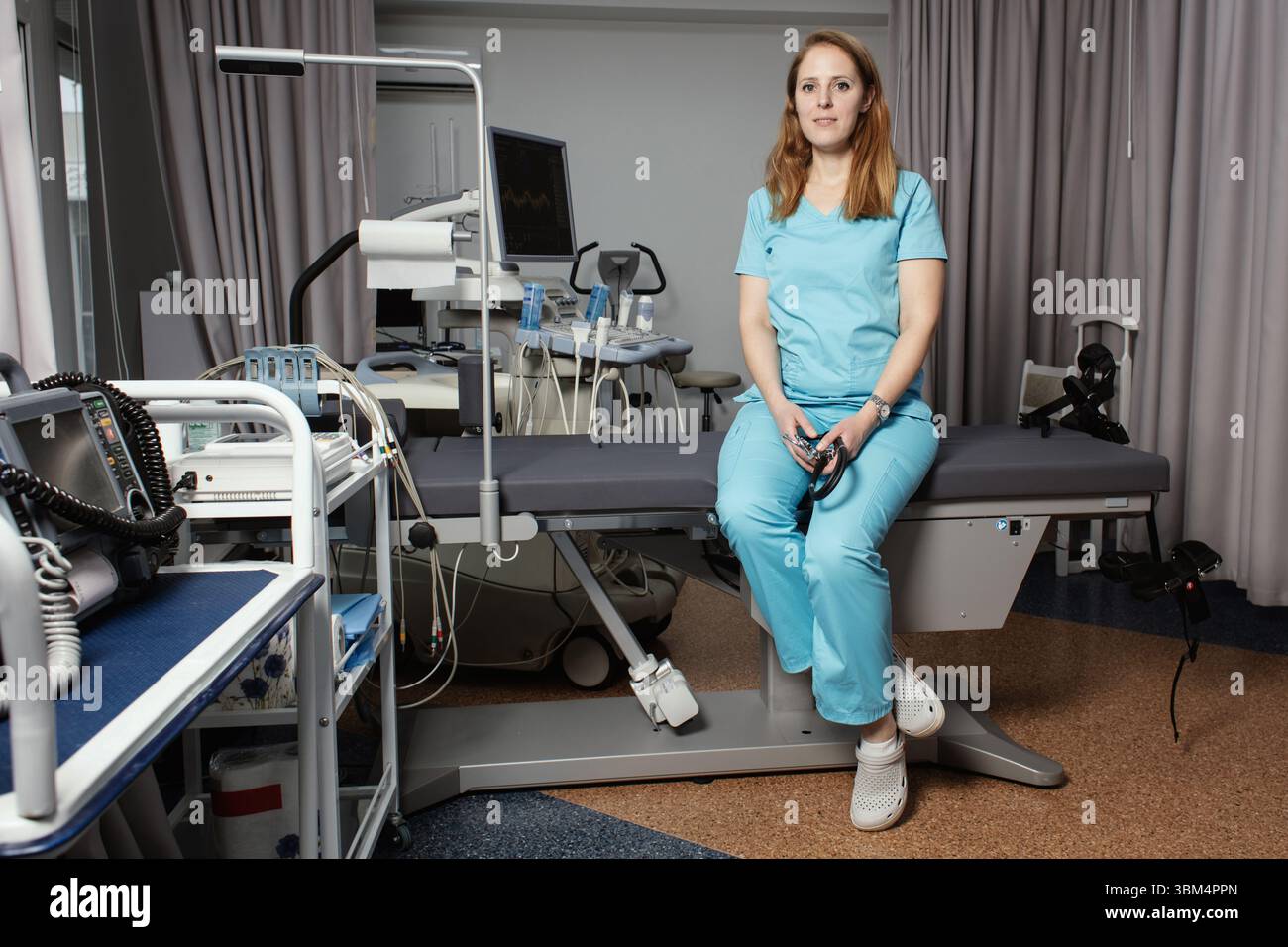 Ritratto di donna medico o ecografo in scrub in piedi nella moderna sala diagnostica a ultrasuoni con attrezzature mediche e stetoscopio. Foto Stock