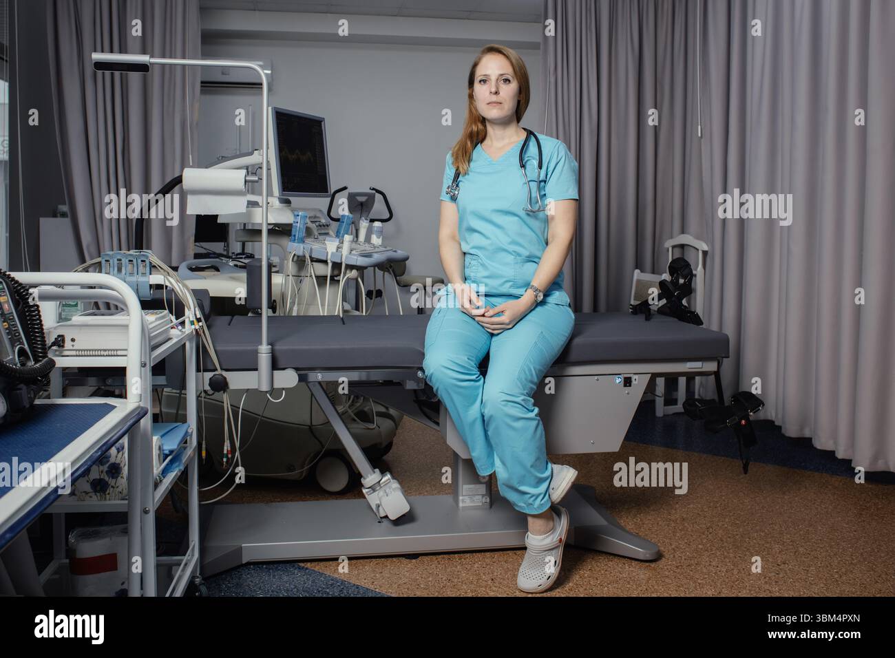 Ritratto di donna medico o ecografo in scrub in piedi nella moderna sala diagnostica a ultrasuoni con attrezzature mediche e stetoscopio. Foto Stock