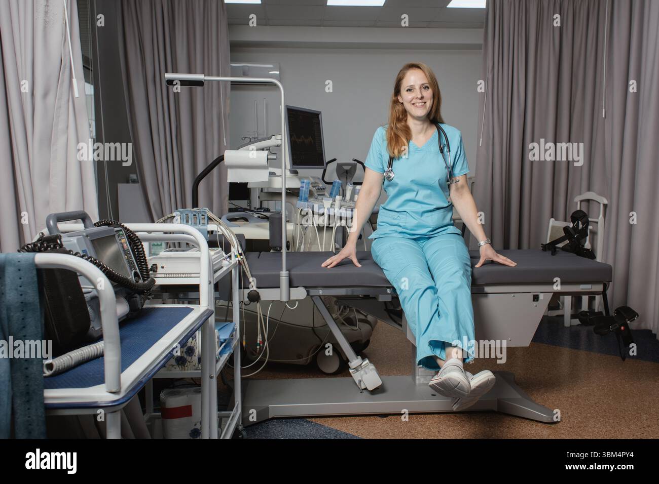 Ritratto di donna medico o ecografo in scrub in piedi nella moderna sala diagnostica a ultrasuoni con attrezzature mediche e stetoscopio. Foto Stock