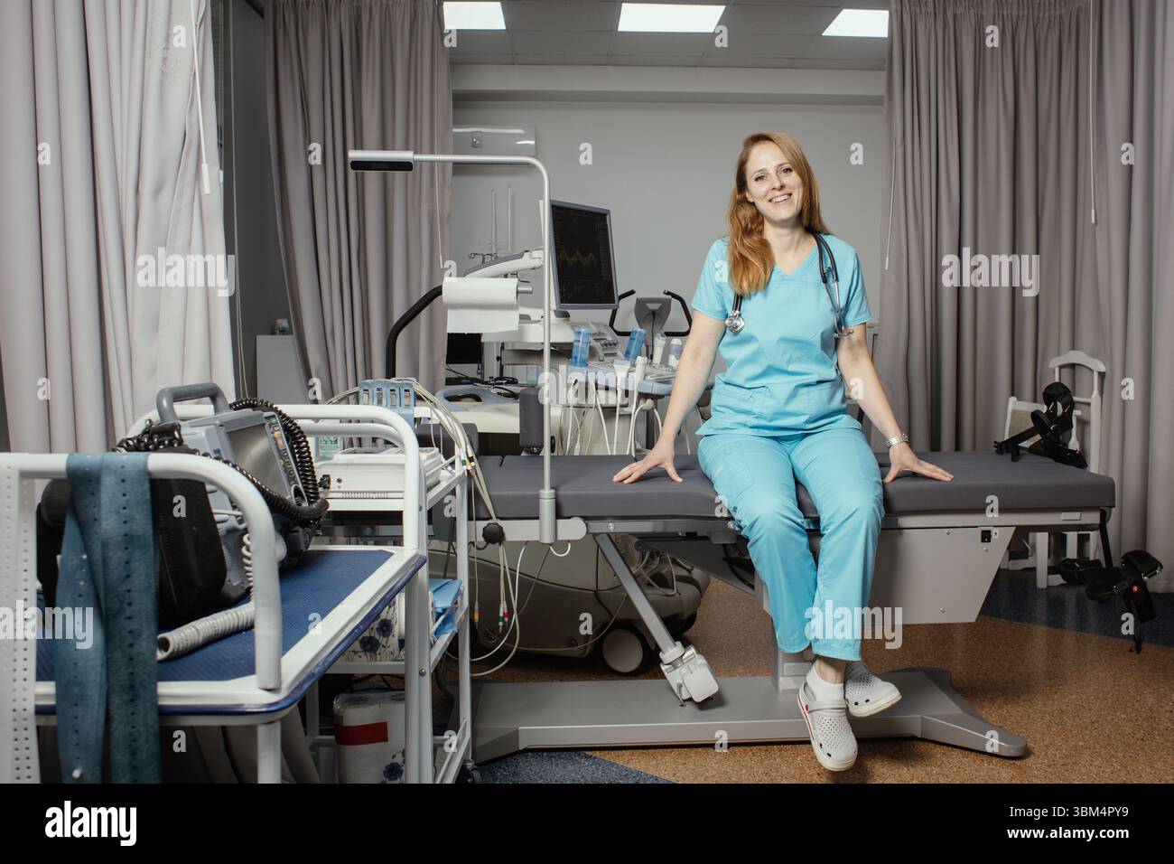 Ritratto di donna medico o ecografo in scrub in piedi nella moderna sala diagnostica a ultrasuoni con attrezzature mediche e stetoscopio. Foto Stock