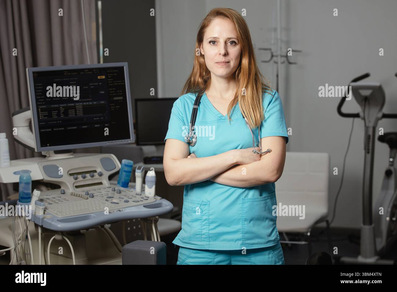 Ritratto di donna medico o ecografo in scrub in piedi nella moderna sala diagnostica a ultrasuoni con attrezzature mediche e stetoscopio Foto Stock