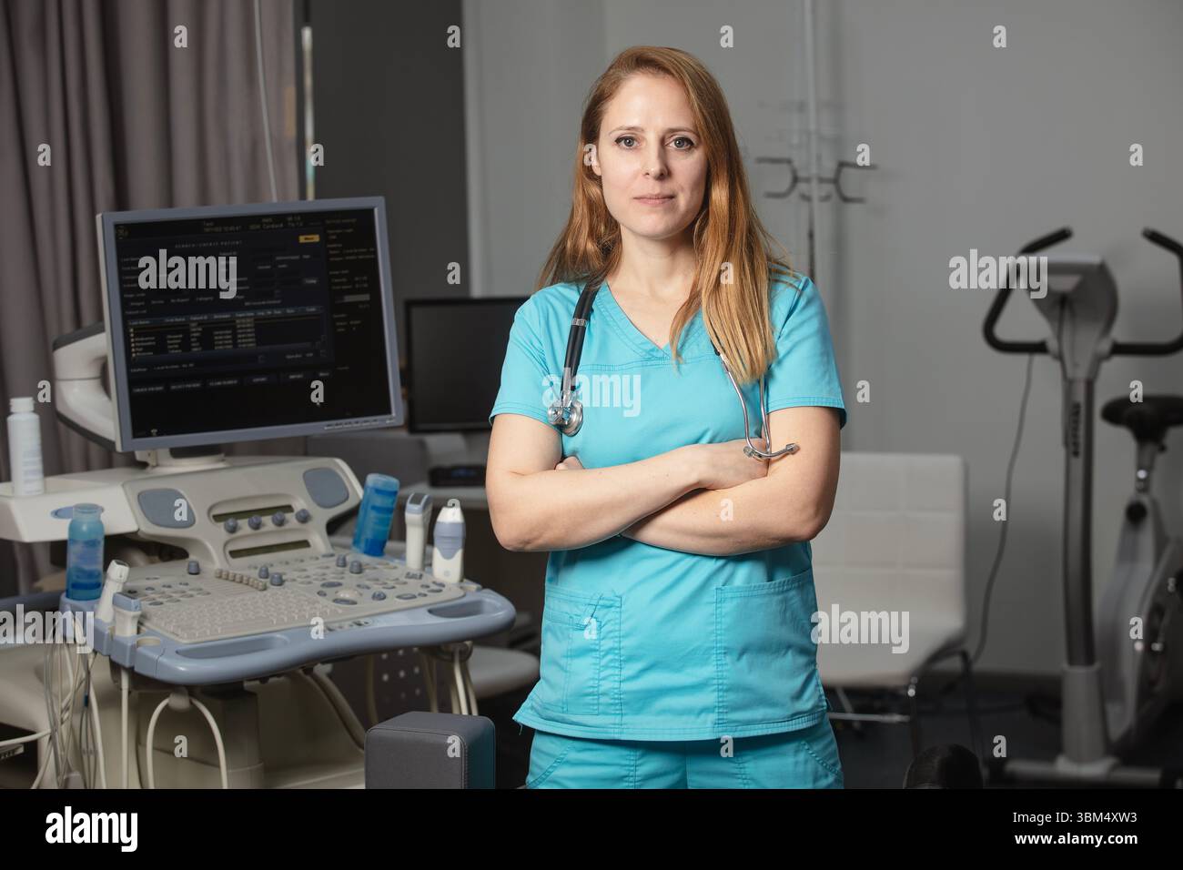 Ritratto di donna medico o ecografo in scrub in piedi nella moderna sala diagnostica a ultrasuoni con attrezzature mediche e stetoscopio Foto Stock