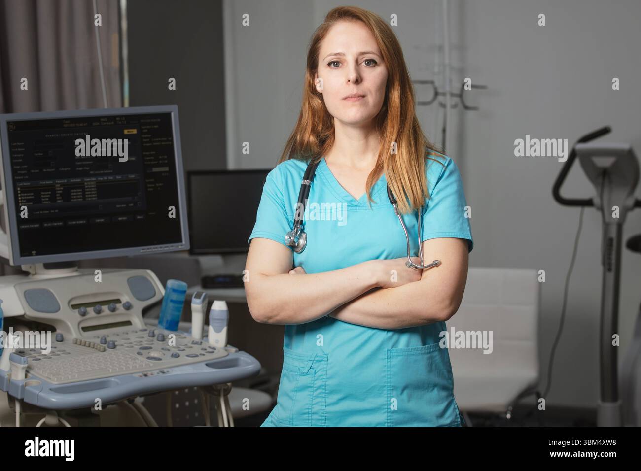 Ritratto di donna medico o ecografo in scrub in piedi nella moderna sala diagnostica a ultrasuoni con attrezzature mediche e stetoscopio Foto Stock