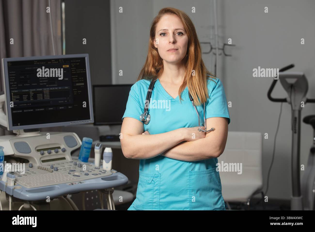 Ritratto di donna medico o ecografo in scrub in piedi nella moderna sala diagnostica a ultrasuoni con attrezzature mediche e stetoscopio Foto Stock