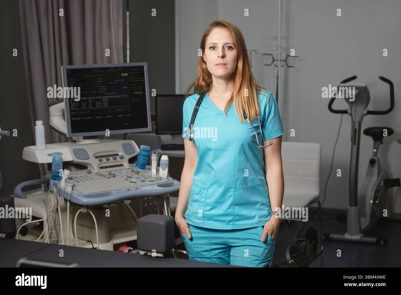 Ritratto di donna medico o ecografo in scrub in piedi nella moderna sala diagnostica a ultrasuoni con attrezzature mediche e stetoscopio Foto Stock
