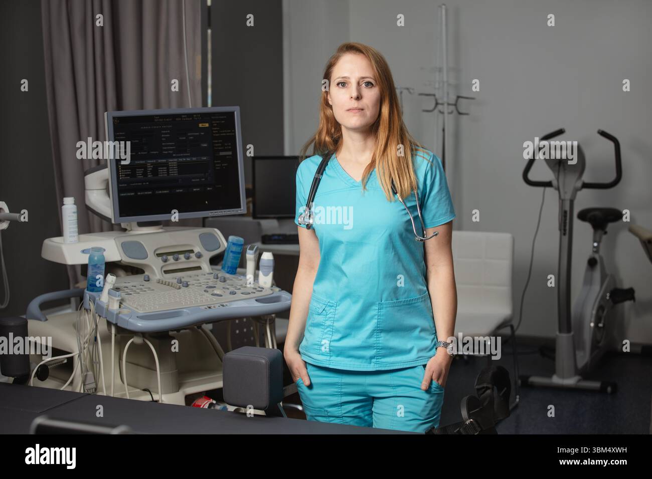 Ritratto di donna medico o ecografo in scrub in piedi nella moderna sala diagnostica a ultrasuoni con attrezzature mediche e stetoscopio Foto Stock