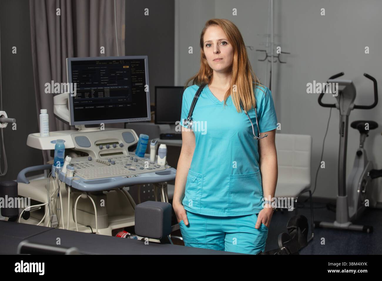 Ritratto di donna medico o ecografo in scrub in piedi nella moderna sala diagnostica a ultrasuoni con attrezzature mediche e stetoscopio Foto Stock