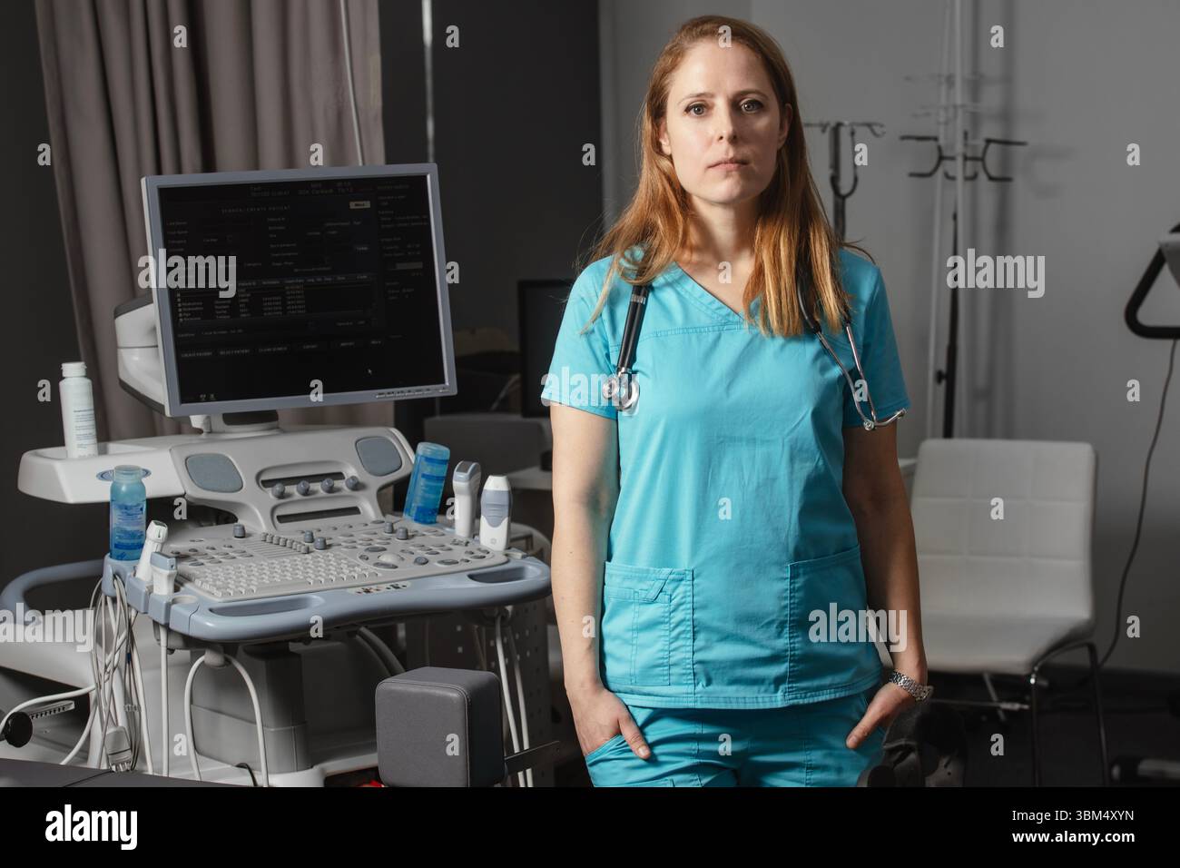 Ritratto di donna medico o ecografo in scrub in piedi nella moderna sala diagnostica a ultrasuoni con attrezzature mediche e stetoscopio Foto Stock