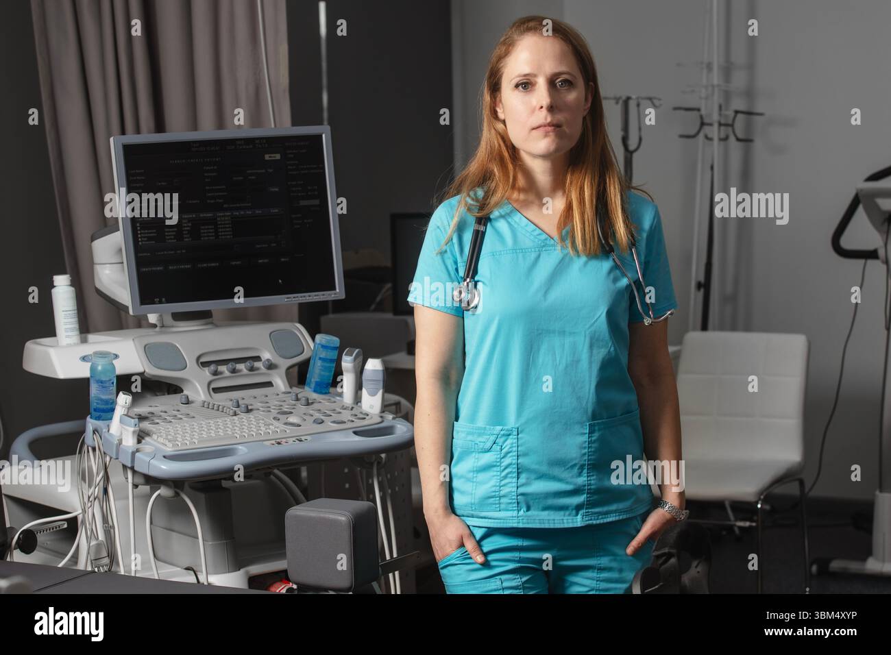 Ritratto di donna medico o ecografo in scrub in piedi nella moderna sala diagnostica a ultrasuoni con attrezzature mediche e stetoscopio Foto Stock