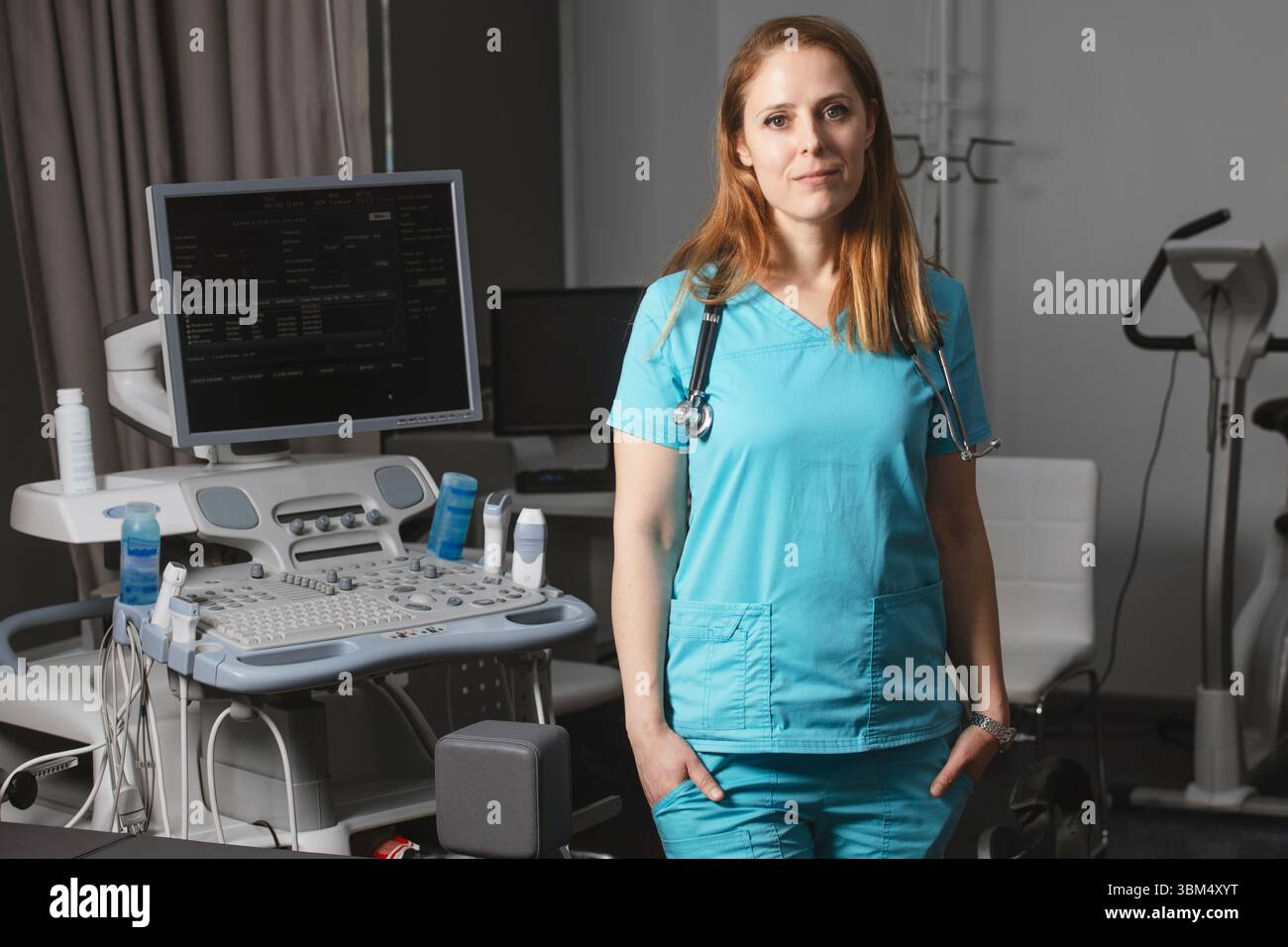 Ritratto di donna medico o ecografo in scrub in piedi nella moderna sala diagnostica a ultrasuoni con attrezzature mediche e stetoscopio Foto Stock