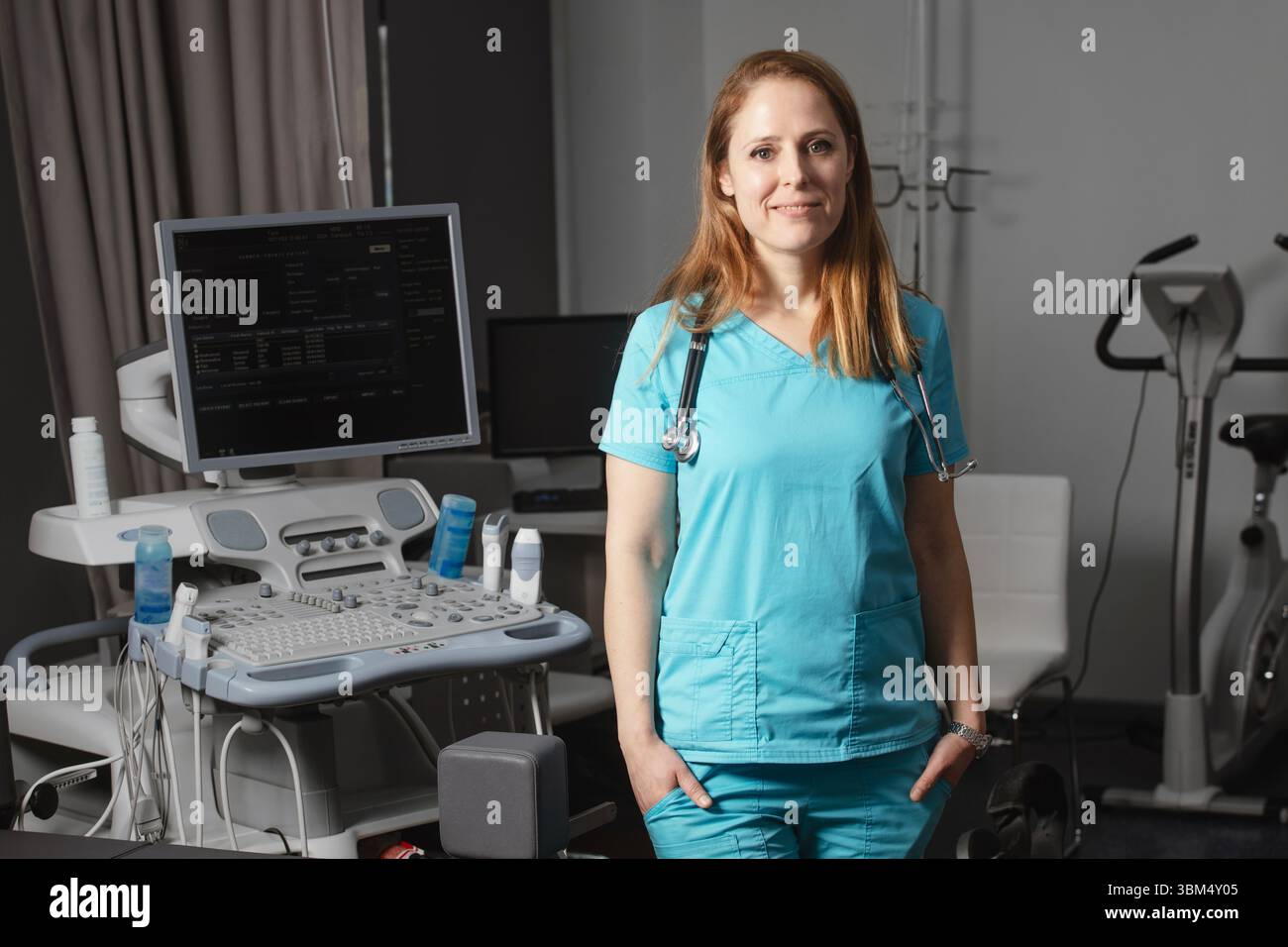 Ritratto di donna medico o ecografo in scrub in piedi nella moderna sala diagnostica a ultrasuoni con attrezzature mediche e stetoscopio Foto Stock