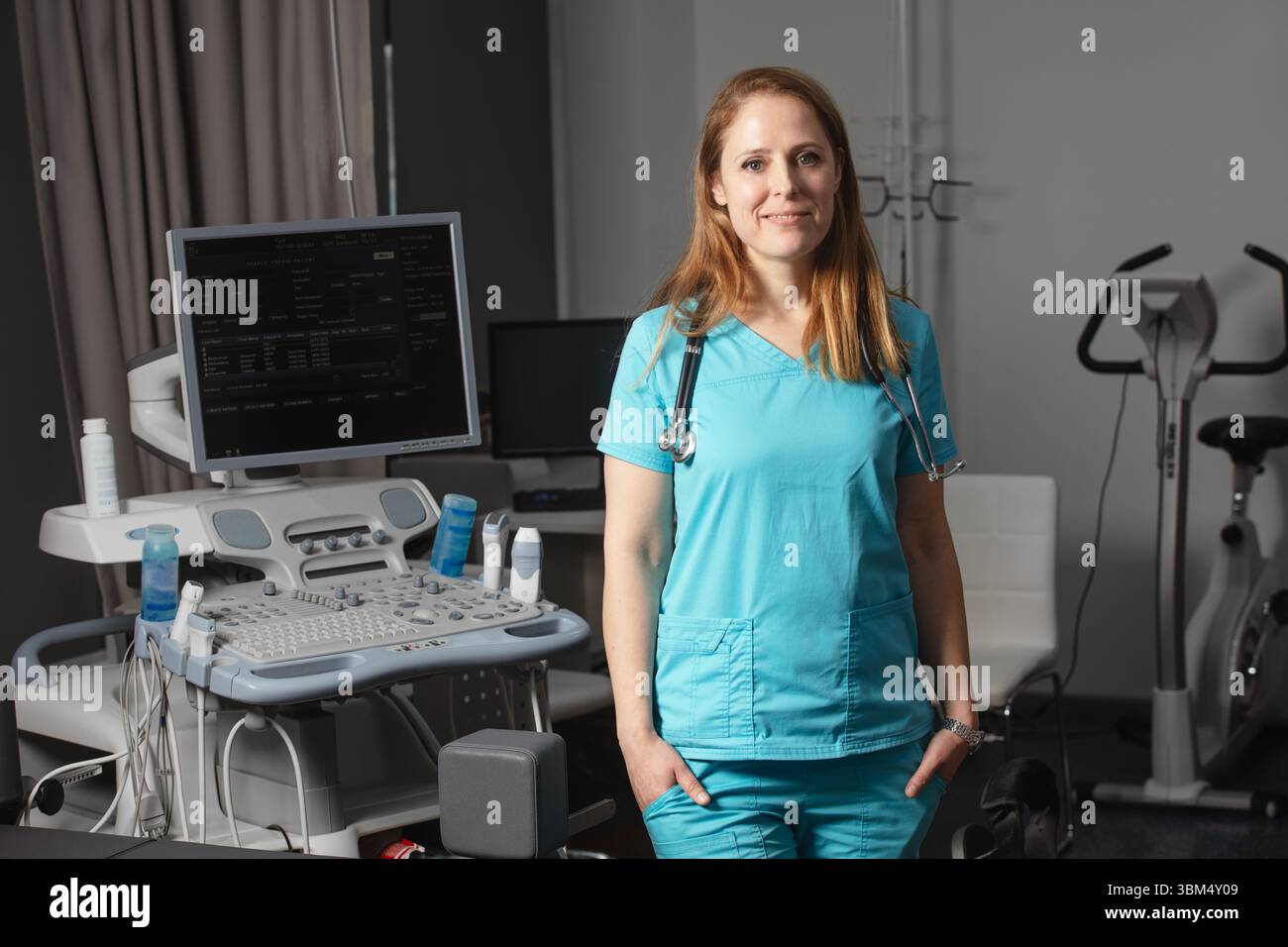Ritratto di donna medico o ecografo in scrub in piedi nella moderna sala diagnostica a ultrasuoni con attrezzature mediche e stetoscopio Foto Stock