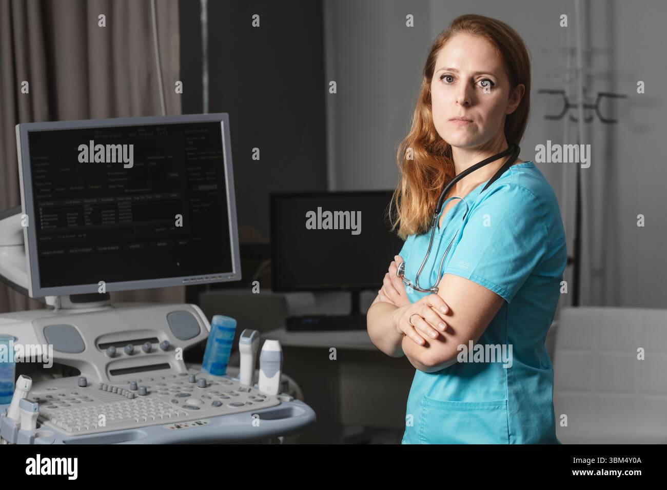 Ritratto di donna medico o ecografo in scrub in piedi nella moderna sala diagnostica a ultrasuoni con attrezzature mediche e stetoscopio Foto Stock