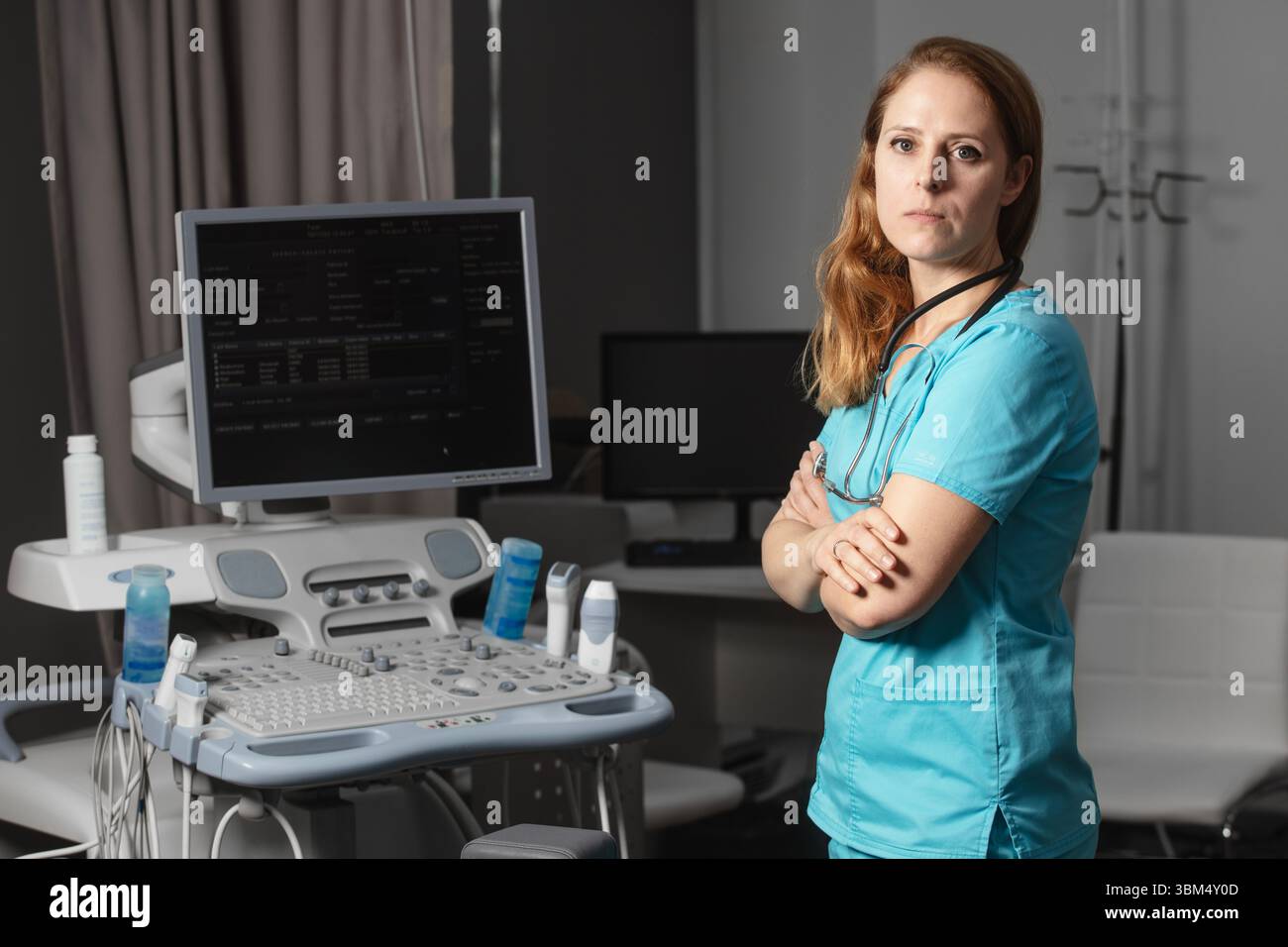 Ritratto di donna medico o ecografo in scrub in piedi nella moderna sala diagnostica a ultrasuoni con attrezzature mediche e stetoscopio Foto Stock
