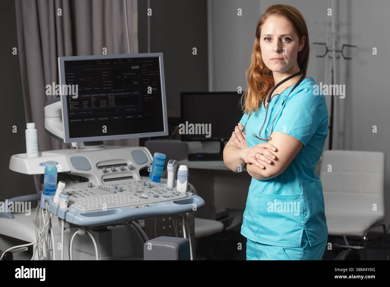 Ritratto di donna medico o ecografo in scrub in piedi nella moderna sala diagnostica a ultrasuoni con attrezzature mediche e stetoscopio Foto Stock