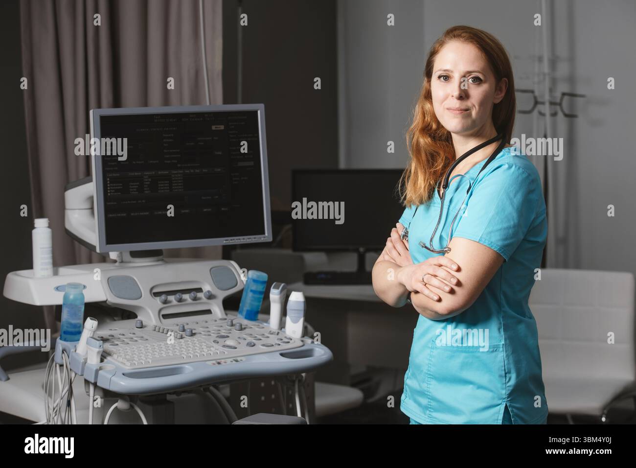 Ritratto di donna medico o ecografo in scrub in piedi nella moderna sala diagnostica a ultrasuoni con attrezzature mediche e stetoscopio Foto Stock