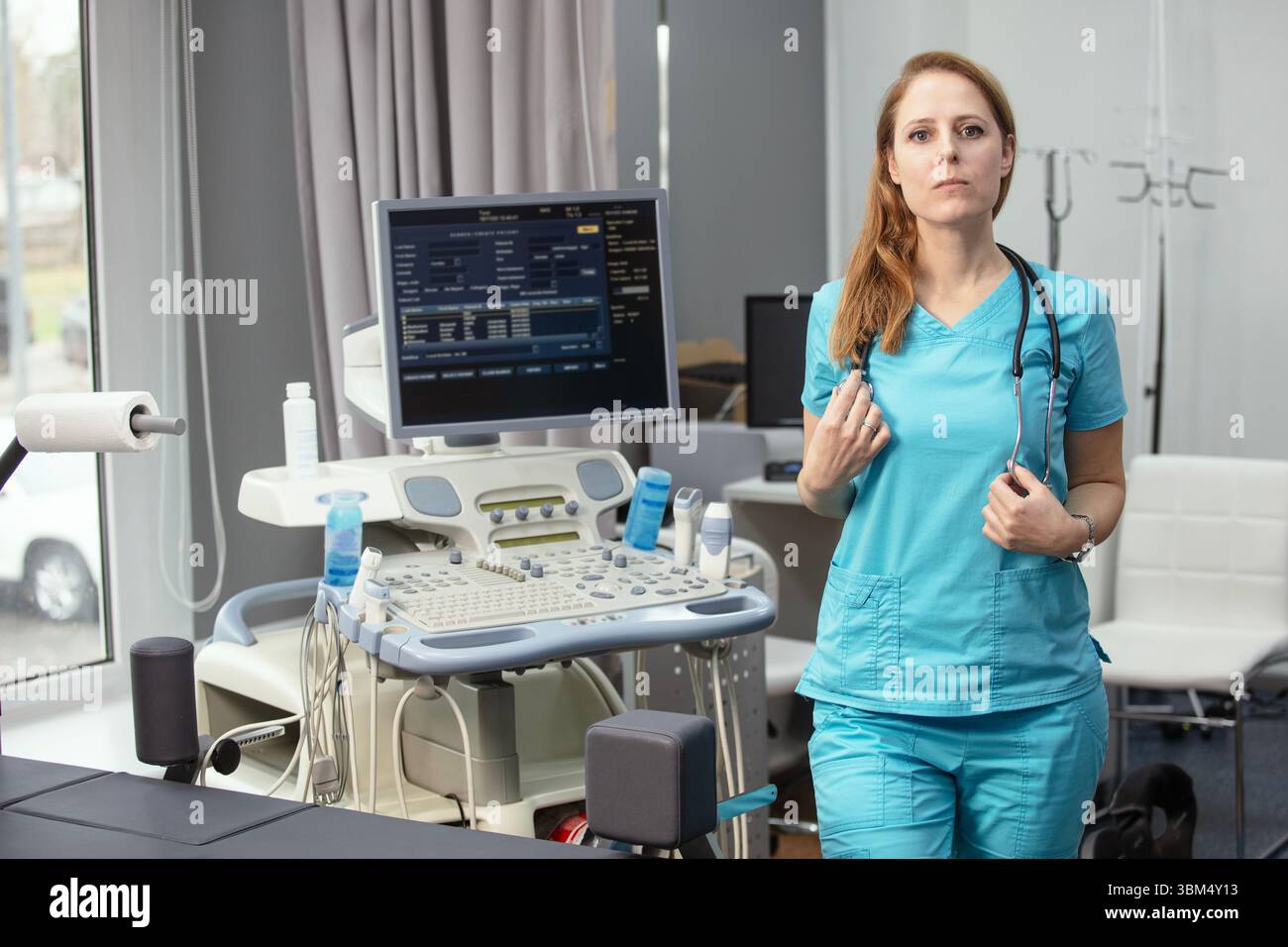 Ritratto di donna medico o ecografo in scrub in piedi nella moderna sala diagnostica a ultrasuoni con attrezzature mediche e stetoscopio Foto Stock