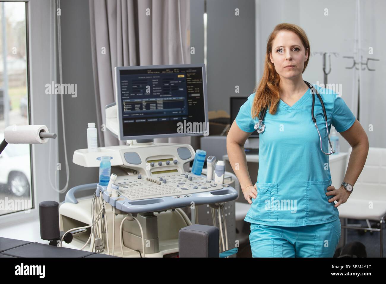Ritratto di donna medico o ecografo in scrub in piedi nella moderna sala diagnostica a ultrasuoni con attrezzature mediche e stetoscopio Foto Stock