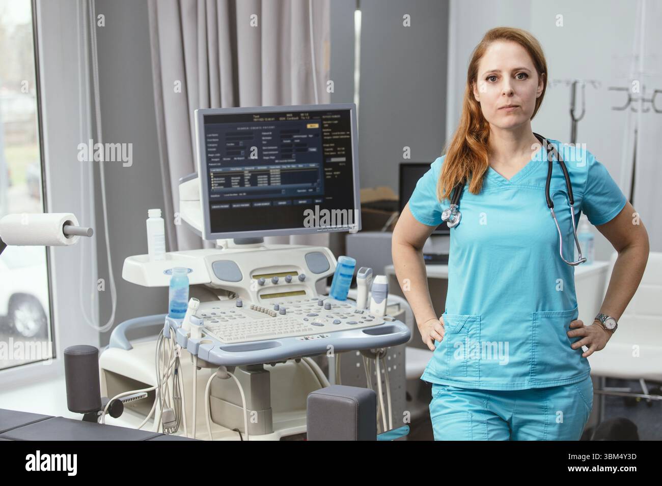 Ritratto di donna medico o ecografo in scrub in piedi nella moderna sala diagnostica a ultrasuoni con attrezzature mediche e stetoscopio Foto Stock