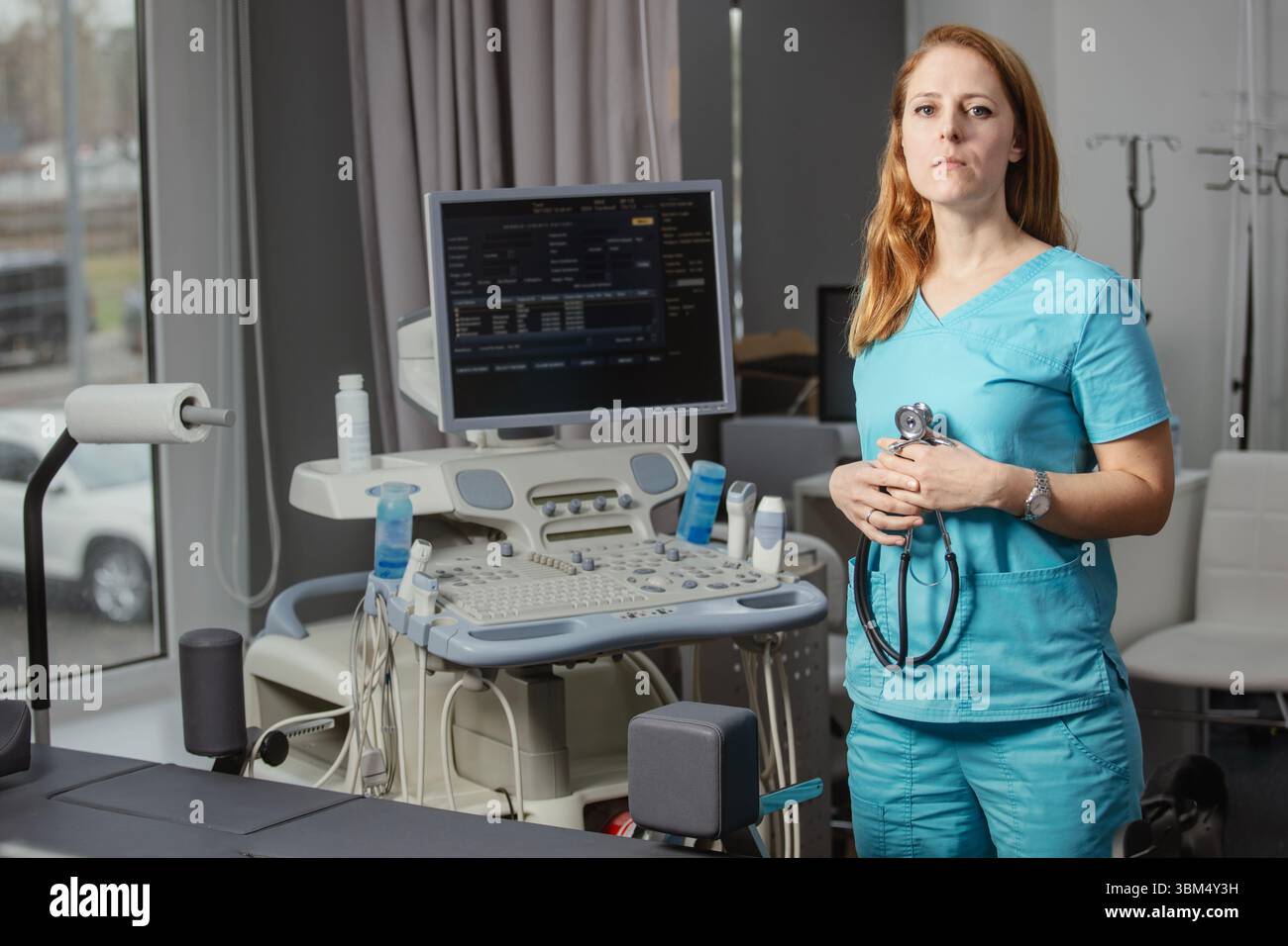 Ritratto di donna medico o ecografo in scrub in piedi nella moderna sala diagnostica a ultrasuoni con attrezzature mediche e stetoscopio Foto Stock